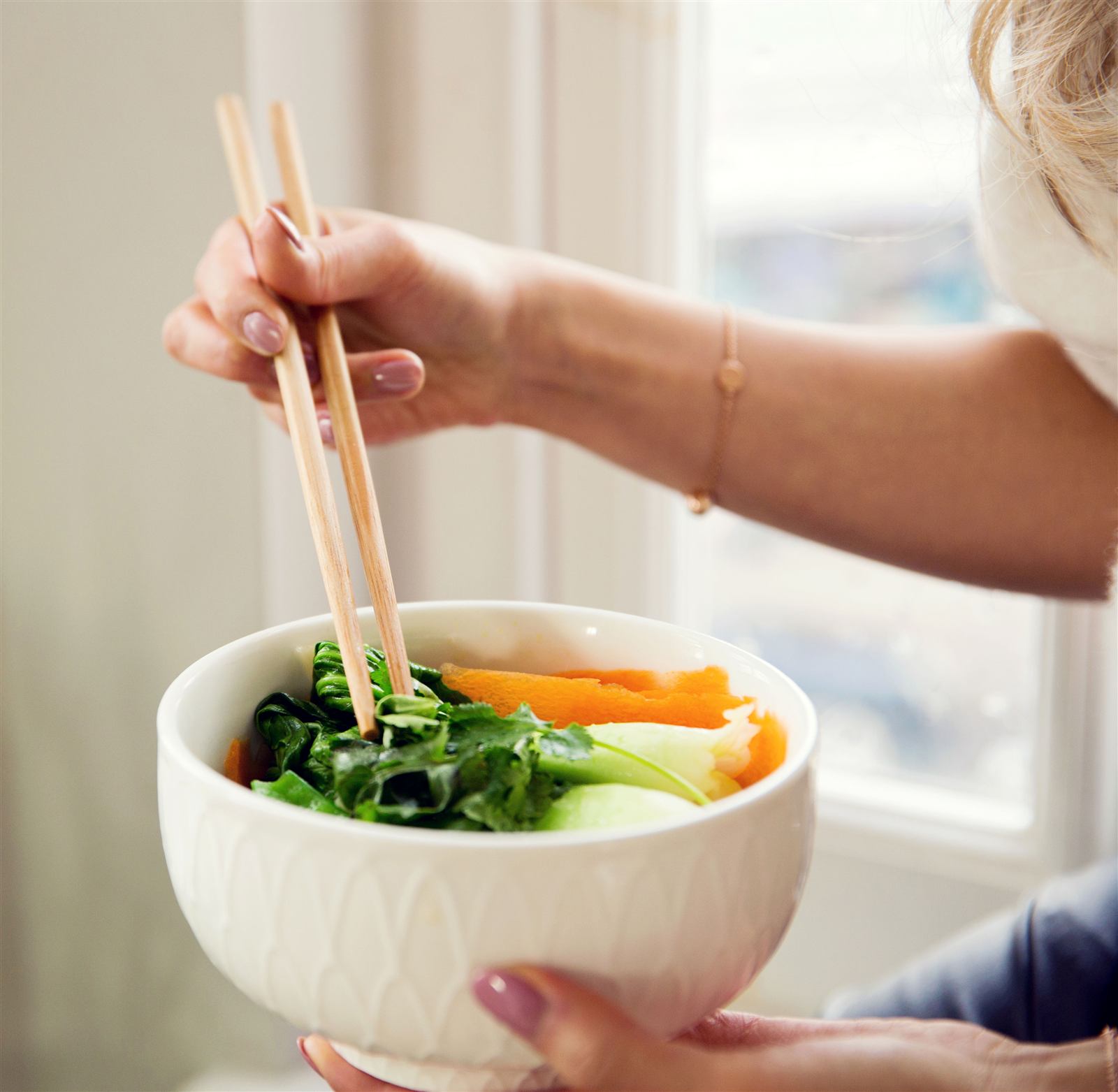 A bowl of fresh greens and vegetables held with chopsticks